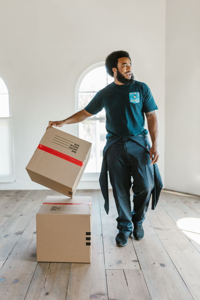 On moving day, a mover carefully carries boxes through a bright, empty room.